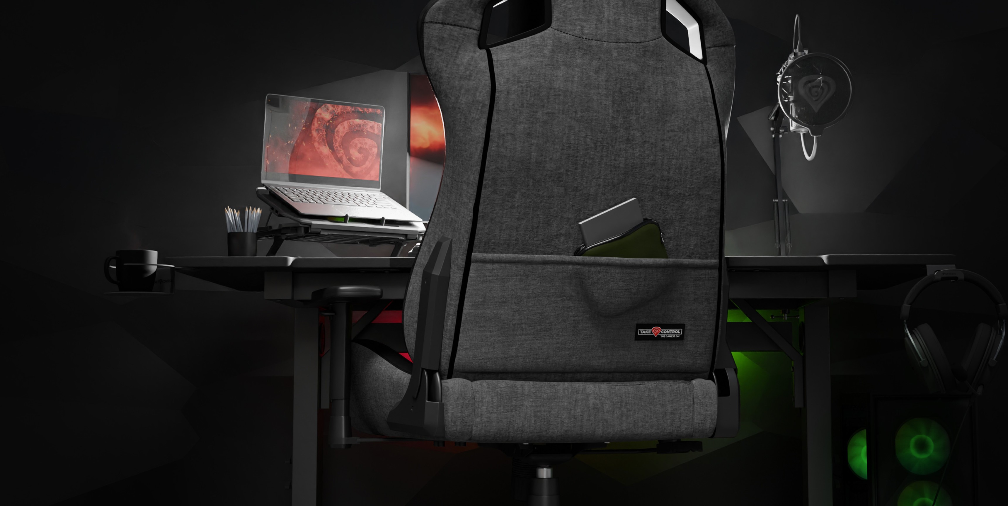 Szary fotel gamingowy Genesis Nitro 660 ustawiony za biurkiem z laptopem i akcesoriami do gier w słabo oświetlonym pomieszczeniu
