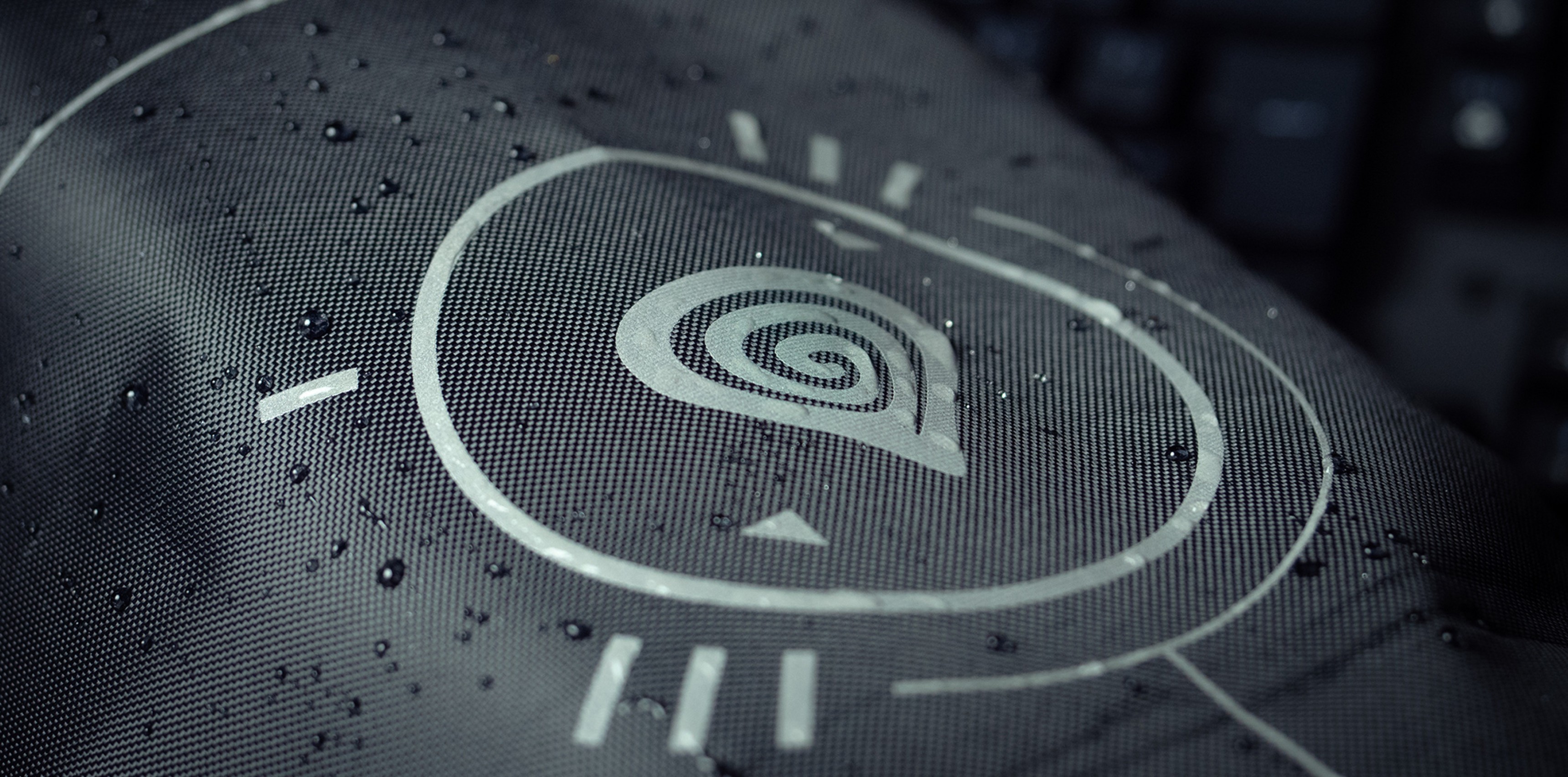 Zbliżenie na tkaninę Genesis Bag G2 przedstawiającą wodoodporną konstrukcję ze spiralnym logo i minimalistycznymi liniami