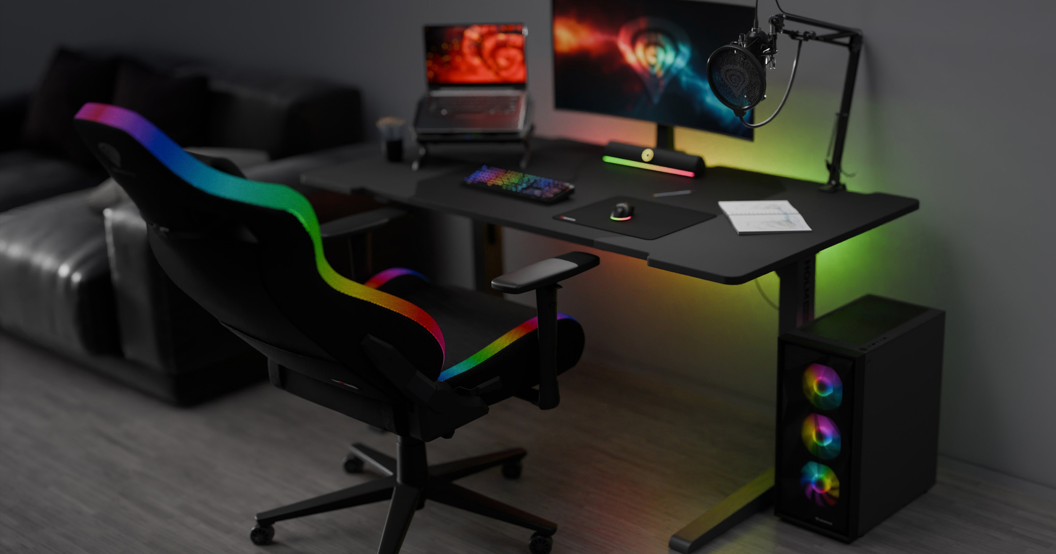Czarny fotel gamingowy z akcentami RGB znajduje się obok eleganckiego biurka z monitorem, klawiaturą i kolorowym zestawem do gier