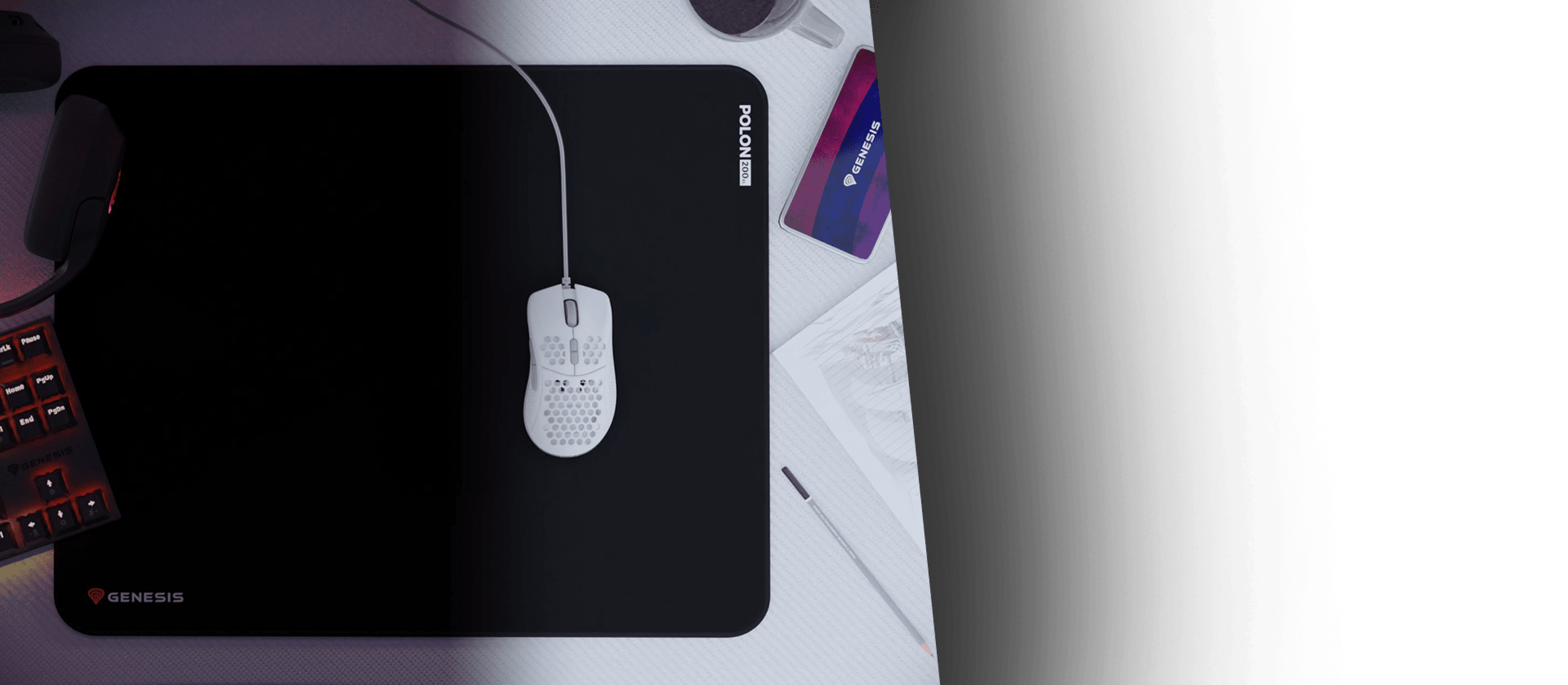 Duża czarna podkładka pod mysz z białą myszką i logo Genesis. W tle widoczne są inne akcesoria gamingowe