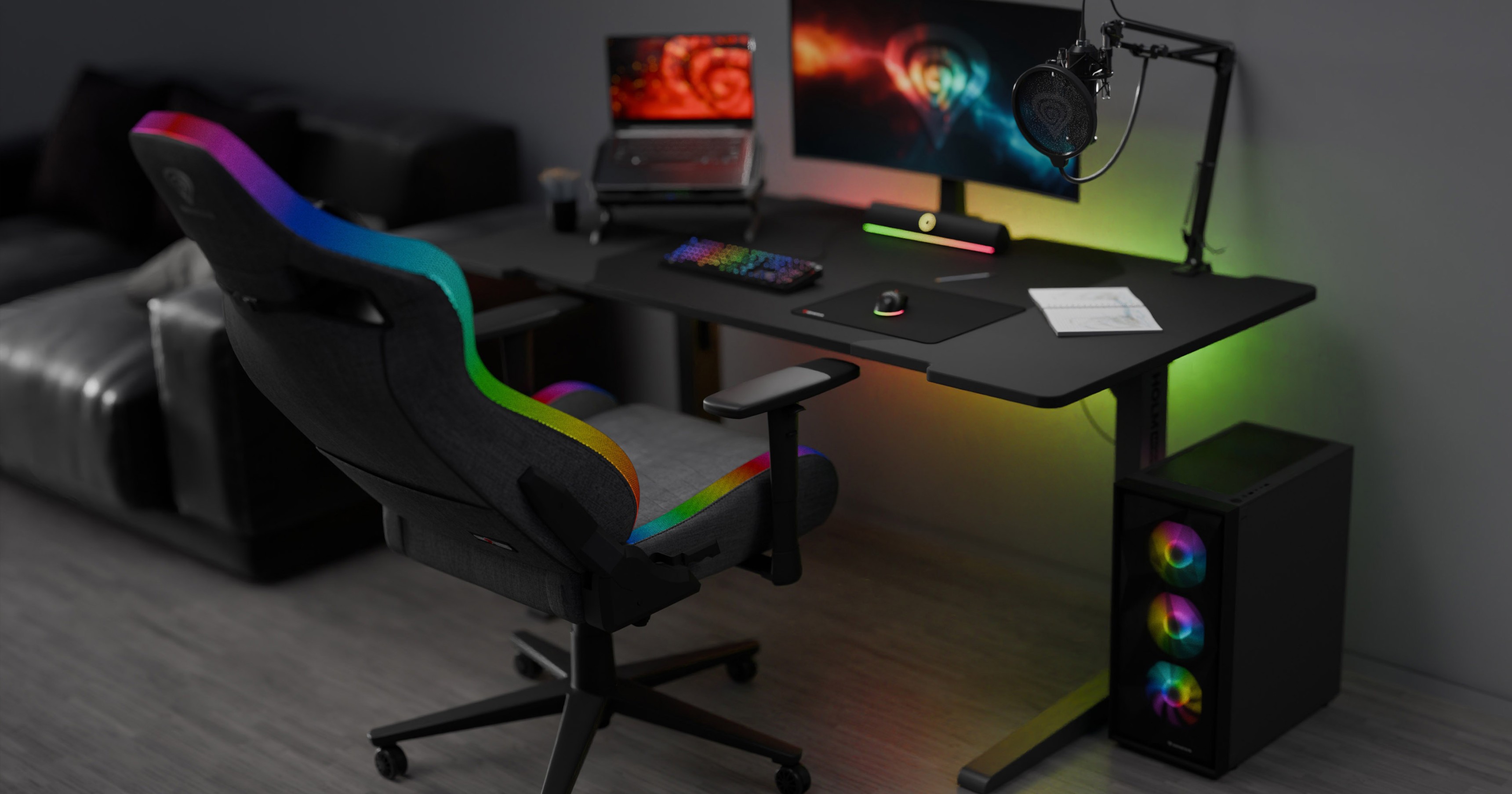 Szary fotel gamingowy z oświetleniem RGB, umieszczony obok eleganckiego biurka do gier, monitora, mikrofonu i akcesoriów do gier.
